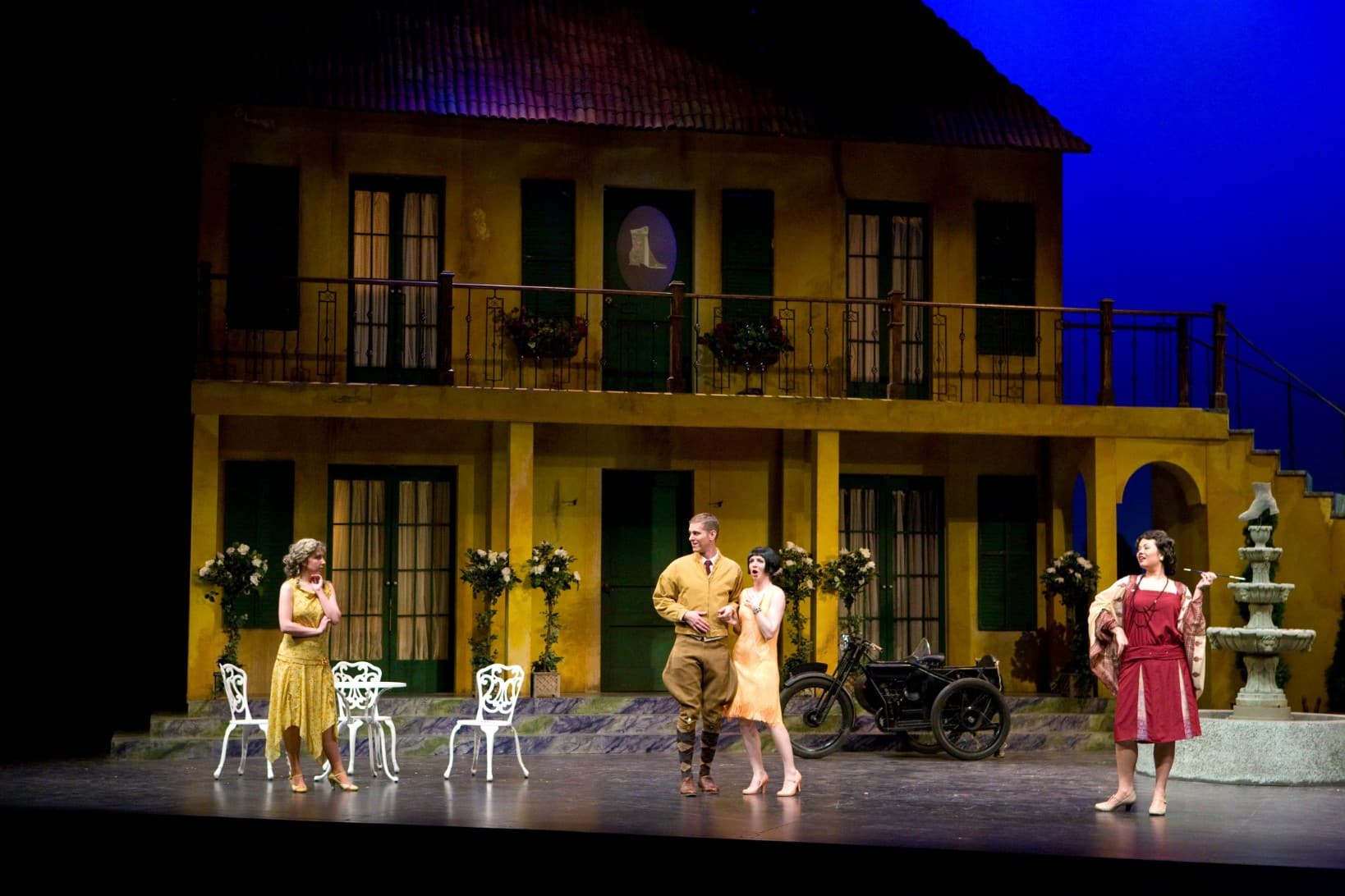 Sarah at center stage in a black wig next to a man. Two women are standing on either side of them, one with a look of amusement
                            on her face.