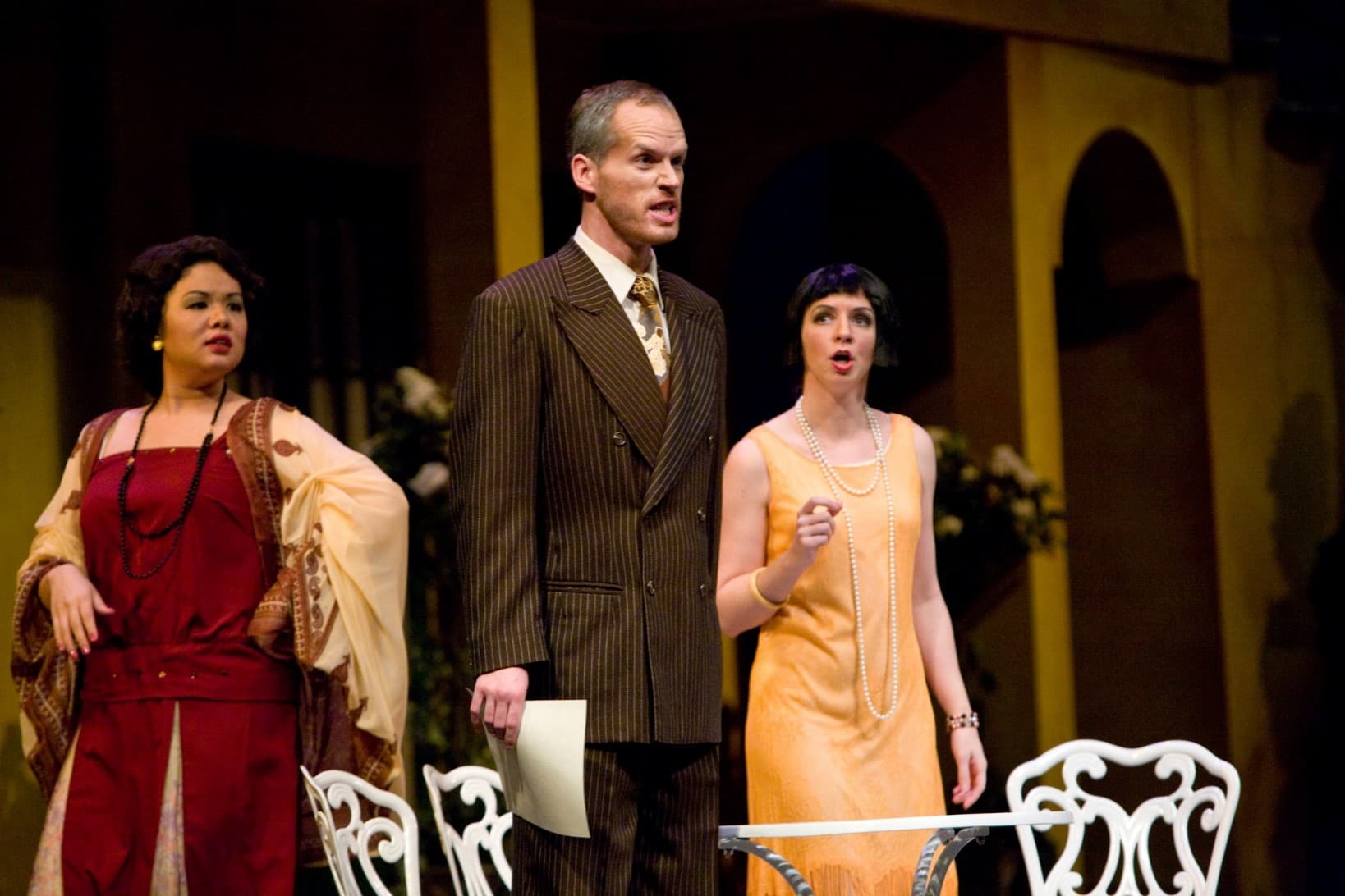 A man is standing holding a paper in one hand with an intense look on his face. A proud woman stands behind him, and a concerned
                            woman stands to the side