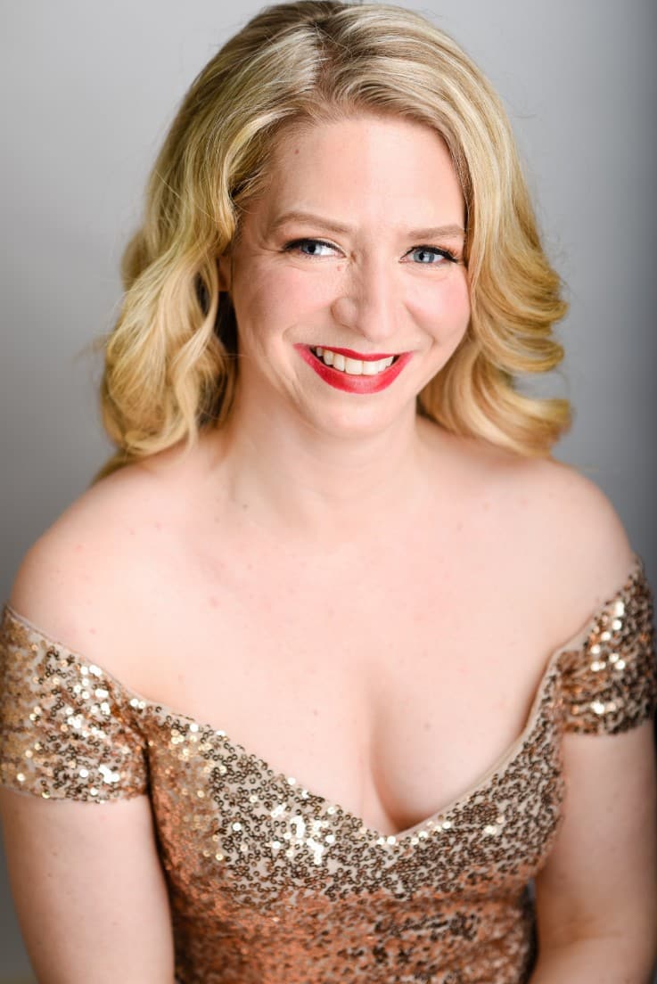 Sarah in her gold sequins dress, smiling at the camera with her head tilted slightly and seated.