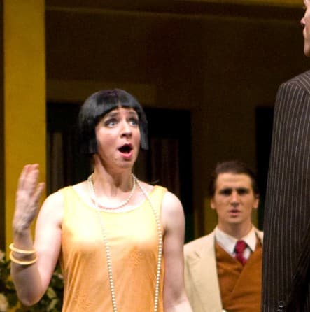 a man has his back to the audience, and Sarah, whose face is to the audience, is singing to him. Other characters on stage look distressed.