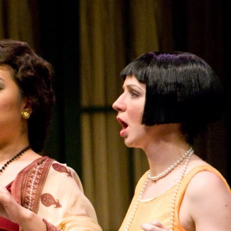 A man is singing with an assertive look on his face. An equally-assertive woman stands behind him, while a third woman is on the side looking concerned.