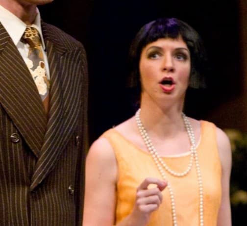 A man is standing holding a paper in one hand with an intense look on his face. A proud woman stands behind him, and a concerned woman stands to the side.