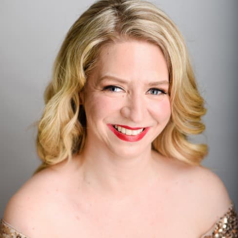 Sarah in her gold sequins dress, smiling at the camera with her head tilted slightly and seated.