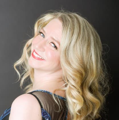 Sarah is wearing a blue sequins dress that has black mesh around the shoulders. Her hair is in curls and she is looking over her shoulder at the camera.