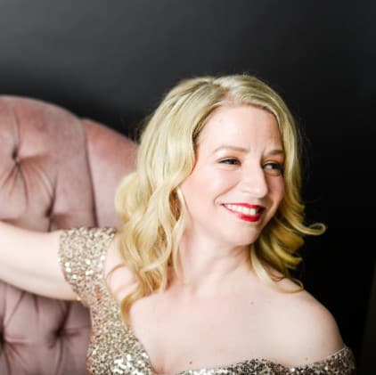 Sarah is in the gold sequins dress and sitting on the couch. she has her right arm on the couch, while her body is centered and her face is looking to her left.