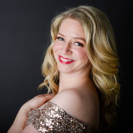 Sarah is wearing her sequins dress and looking over her shoulder with on hand on her heart.