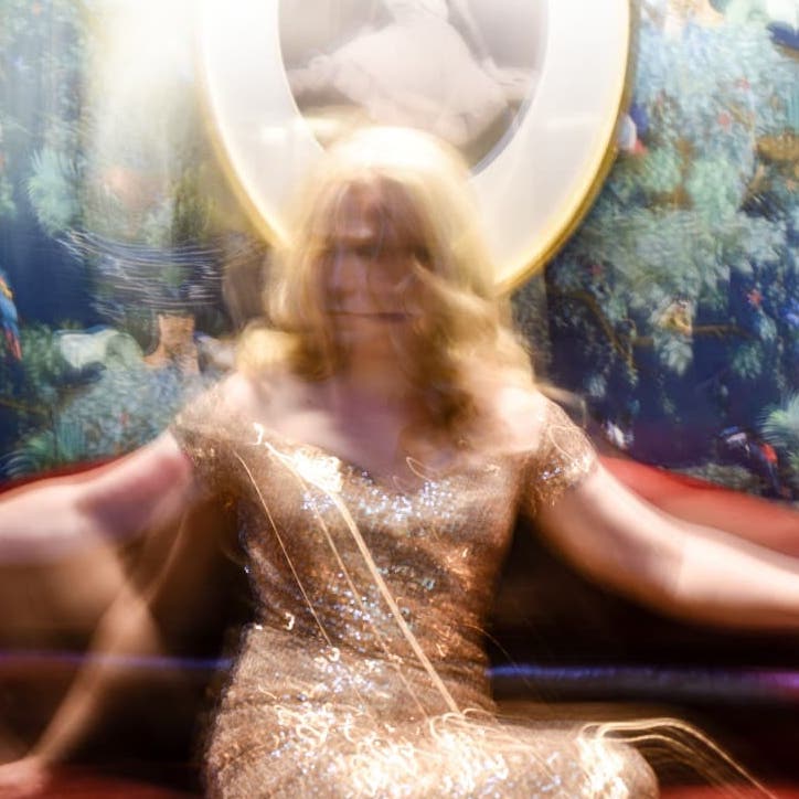 Sarah is in her gold sequins dress and sitting on a red leather couch. The entire picture is blurry, and the highlight of the image is the colours as opposed to the details. It looks like a whirlwind of colours and lights.