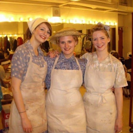 Three women are standing in the middle of a dressing room in costume - they are wearing chef's aprons.